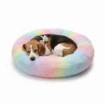 Plush donut pet bed with rainbow tie-dye pattern, with two dogs curled