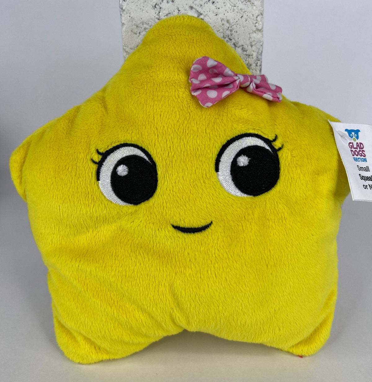 Yellow plush wedge dog toy with embroidered eyes, small bow detail, tag