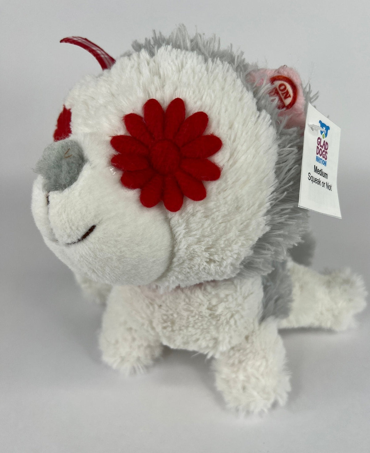 White plush dog toy with red flower patch and red squeaker antenna, tag