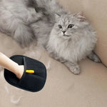 Black pet grooming mitt with yellow tab beside gray cat, ready for hair removal