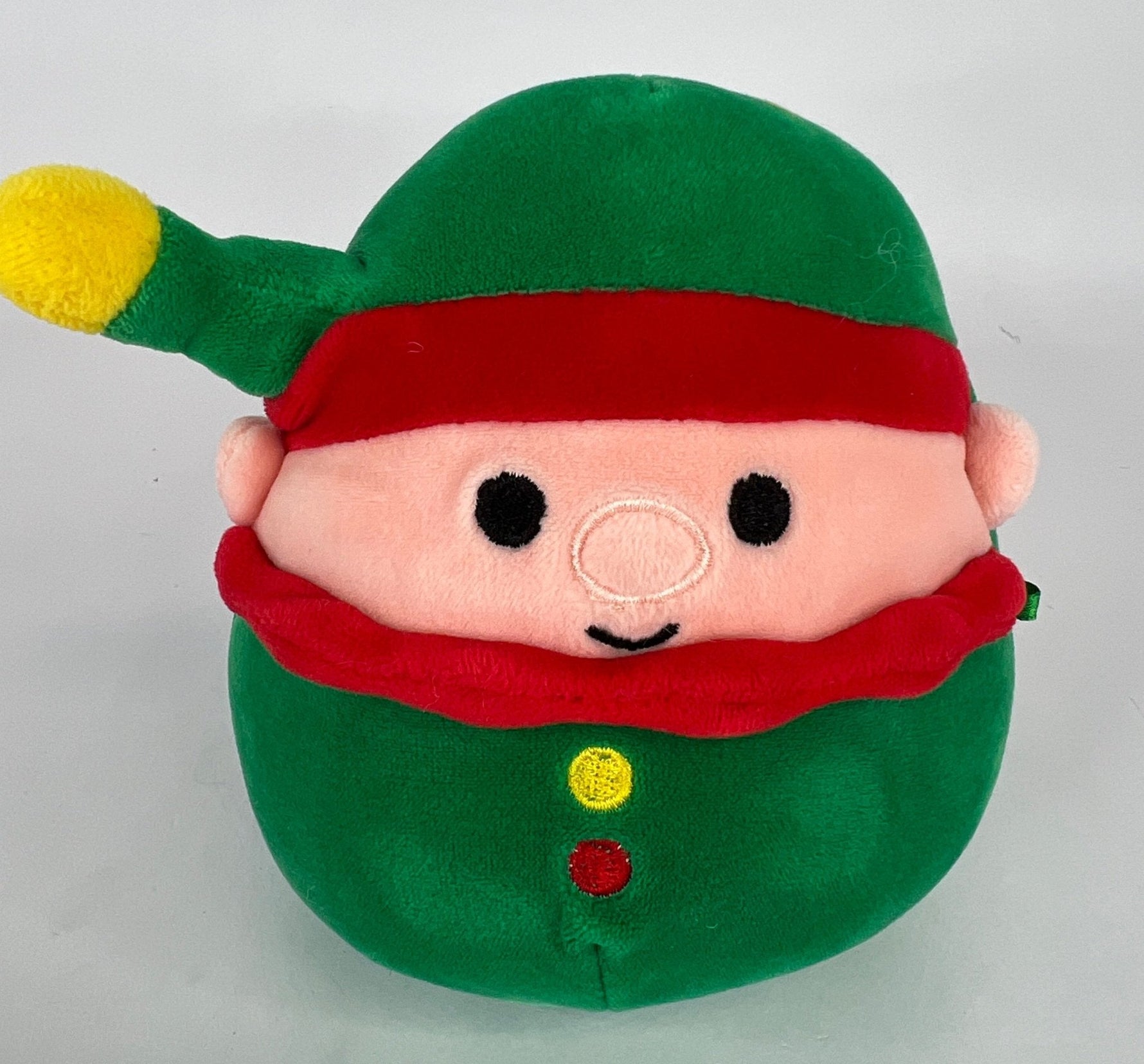 Green holiday elf plush with red hat band, cute face, and small button details