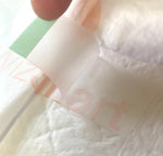 Training pad with top sheet texture and a green adhesive tab, close-up detail