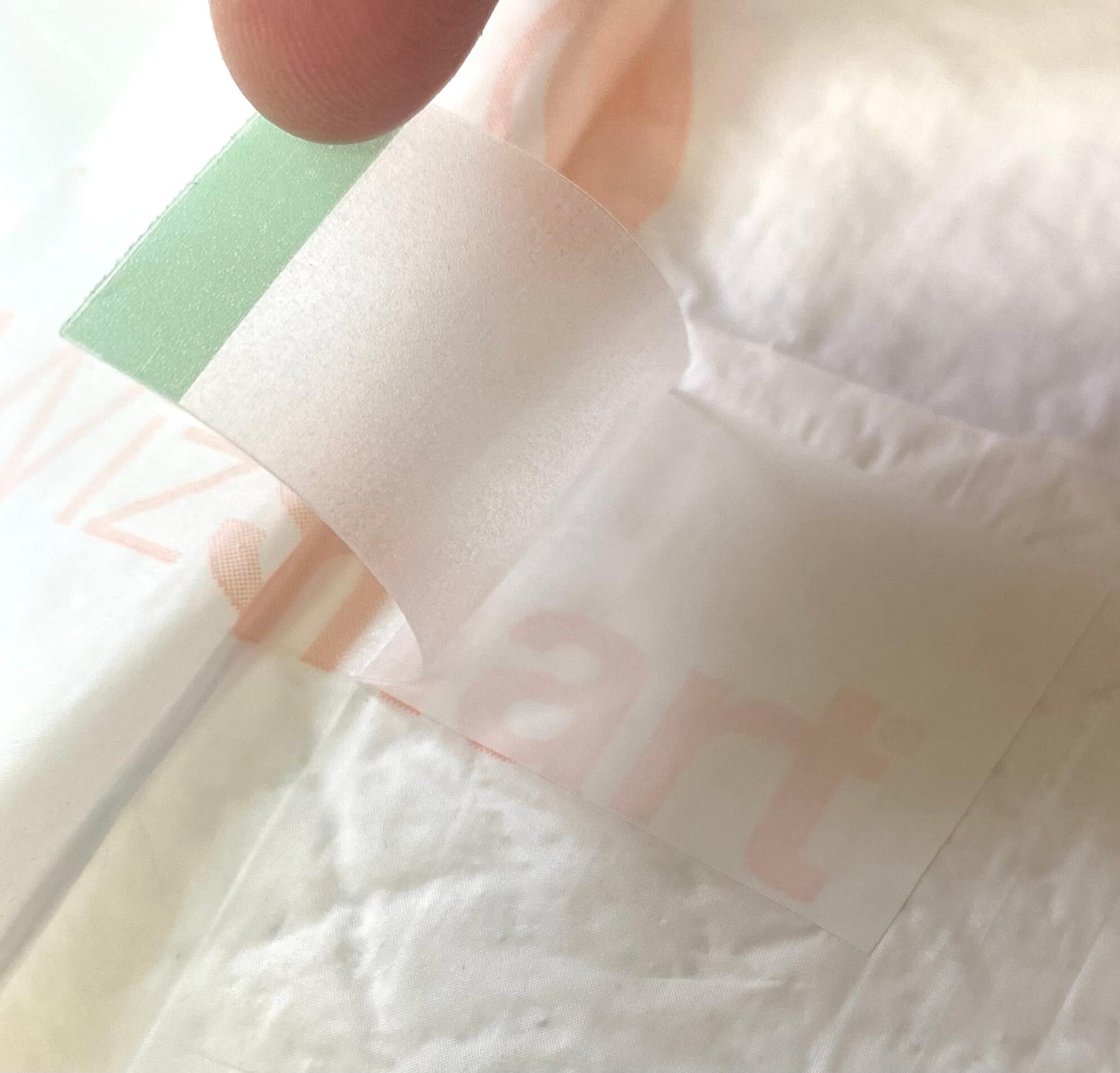 Training pad with top sheet texture and a green adhesive tab, close-up detail